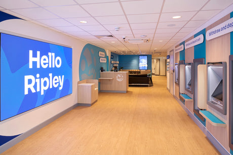 Interior of a store with 'Hello Ripley' sign on a large screen, checkouts, and ATM machines.