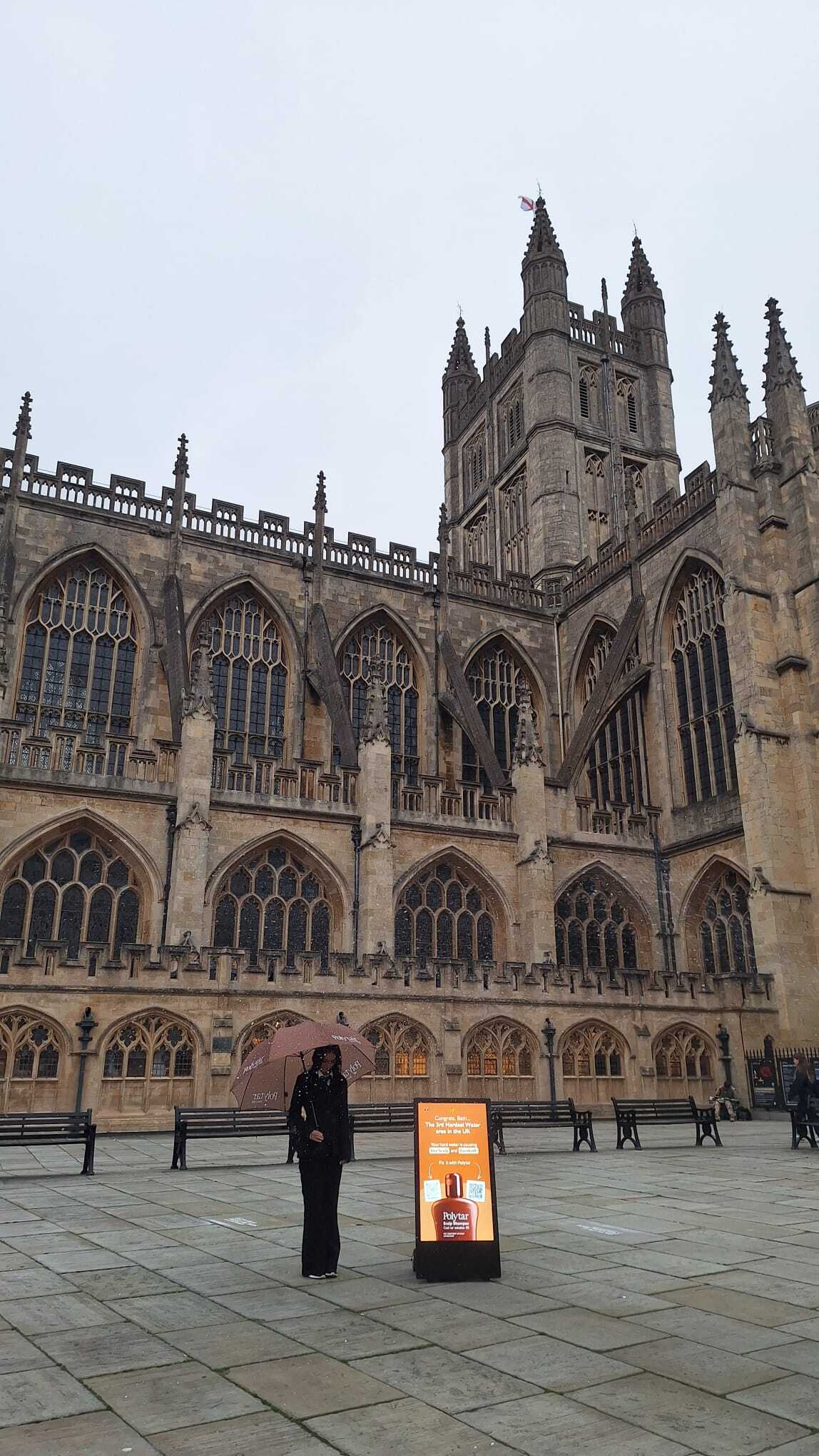 Large gothic cathedral with a person standing in front of it on a cloudy day.